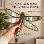 Hand holding an antique bronze dragonfly mirror near a wall